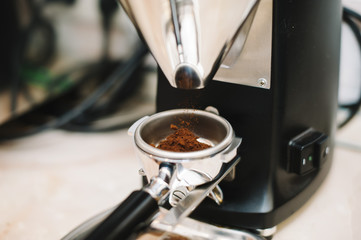 freshly ground coffee beans in a portafilter by the coffee grinder