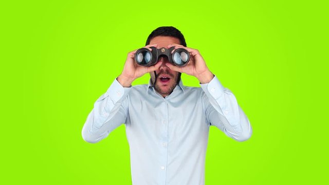 Astonished young man using a binoculars against green background