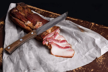 Puff smoked bacon and knife on the packaging paper. Vintage naturmort in a rustic style.