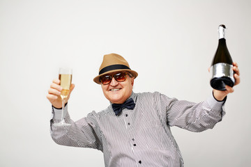 Waist-up portrait of dressed-up elderly man dancing with glass and bottle of champagne and smiling at camera cheerfully © pressmaster
