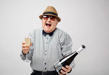 Waist-up portrait of dressed-up retired man holding a bottle of champagne and laughing cheerfully...