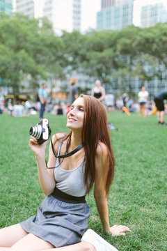 Young woman holding camera while sitting on grass