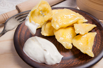 Close up view of boiled varenyky or dumpling with cottage cheese or curd on metal fork. Fresh boiled homemade ukrainian dumplings on clay plate and with sour cream on wooden background..
