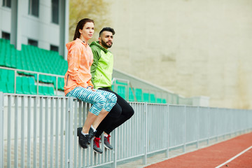 Obraz premium Young athletes, man and woman, wearing bright colorful sportswear sitting, resting on railings after running practice in stadium