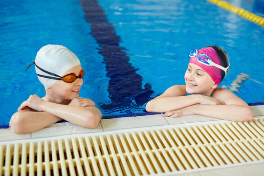 Cheerful boy and girl smiling and talking while taking a break after swimming holding onto pool border