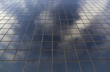 pattern of square black ceramic tiles with reflecion of sky and clouds