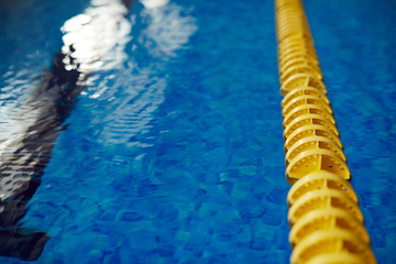 Closeup image of yellow line in clear rippling blue water of swimming pool
