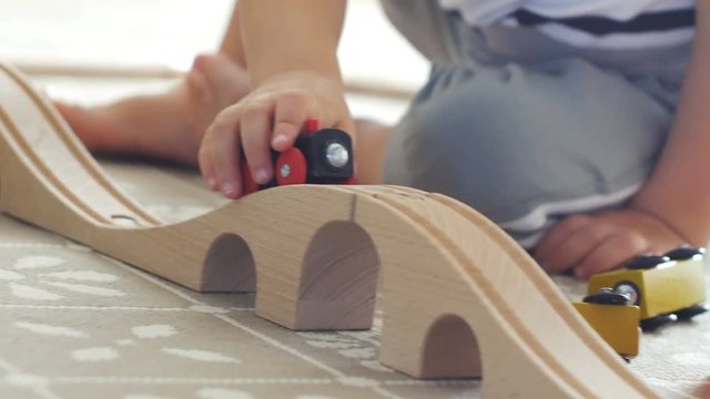 Two years old boy plays with wooden railroad in a sunny room