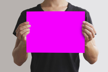 Man in black t shirt holding blank pink A4 paper horizontally. Leaflet presentation. Pamphlet hold hands. Man show clear offset paper. Sheet template. Isolated on grey background