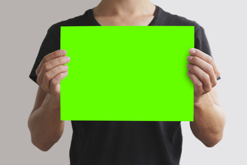 Man in black t shirt holding blank green A4 paper horizontally. Leaflet presentation. Pamphlet hold hands. Man show clear offset paper. Sheet template. Isolated on grey background