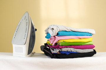 Iron stands with stacks of ironed colored linen. Pile of clothes. Ironing concept. All colors of...