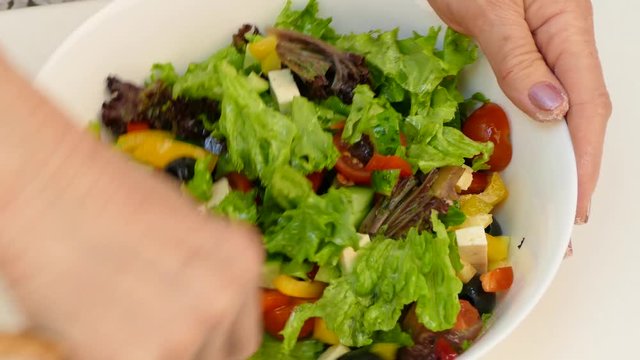 Female hands mix the salad in a large white bowl.