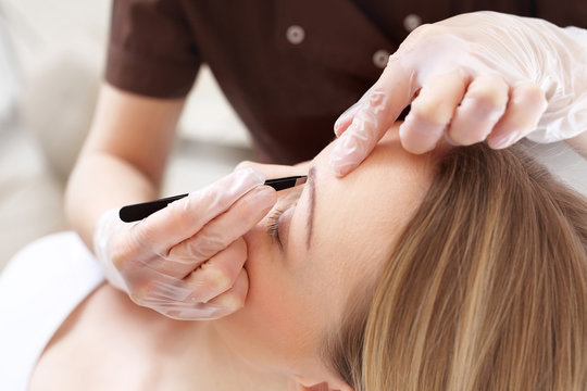 Regulacja brwi pęseta.
Kosmetyczka depiluje brwi klientki nadając im odpowiedni kształt
