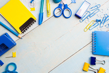 School stationery products such as paper clips, pins, notebooks, pens, pencils, rulers, scissors lying on blue wooden table with space to write your ad text