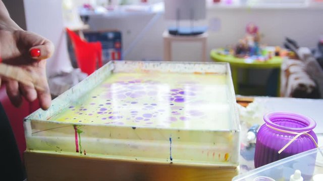 Process of painting - purple paint drops on yellow background - woman draws on water in Liquid Ebru art technics
