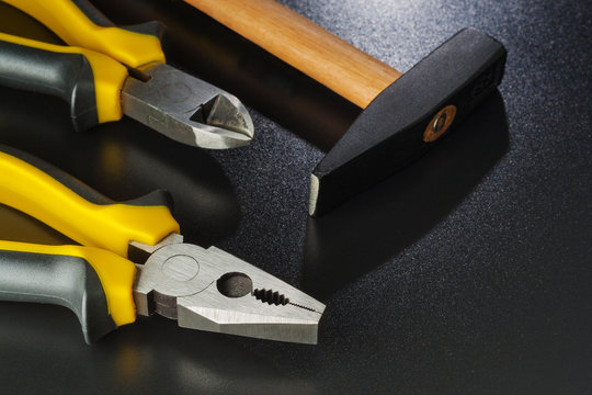 Pliers, hammer with brass screws on dark table.