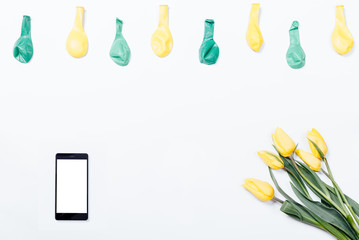 Yellow flowers, mobile phone, and balloons on a white table