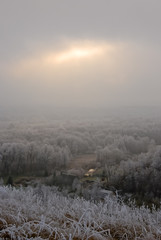 Winter landscape with sun shining through clouds and noarfrost covered trees