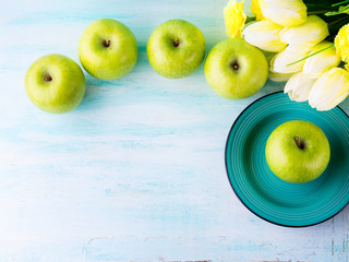 Green pastel background with apples flowers. Healthy food concept backdrop for writing text. Top view