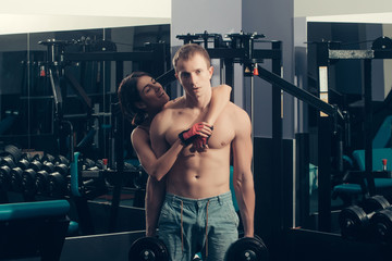 muscular man and smiling happy girl at gym with dumbbells