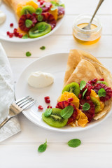 Thin crepes with fresh kiwi, orange, sicilian orange, honey, cream and mint leaves on white rustic wooden table. Selective focus