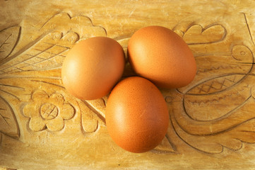 Three brown eggs on a carved wooden base
