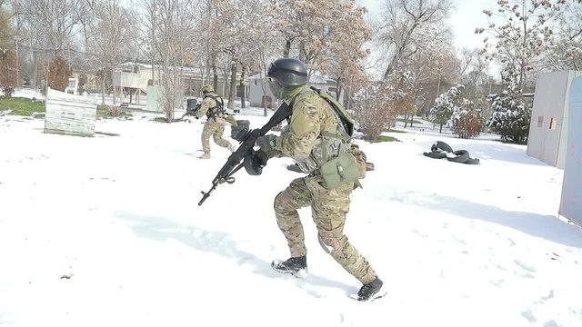 Two boys run and play airsoft. The player is in the snow, and fired from automatic weapons. Play airsoft in the winter