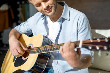 Cropped shot of young handsome man playing guitar and smiling