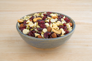 Nuts and fruit trail mix in an old stoneware bowl atop a wood table.