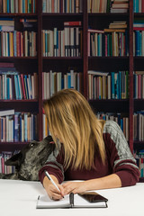 Woman sitting at  a table writing with a dog next to her trying to get attention.