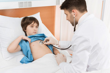 Obraz premium doctor in medical uniform examining little boy with stethoscope
