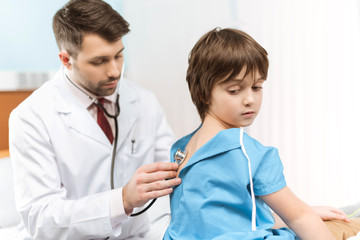 doctor in medical uniform examining little boy with stethoscope