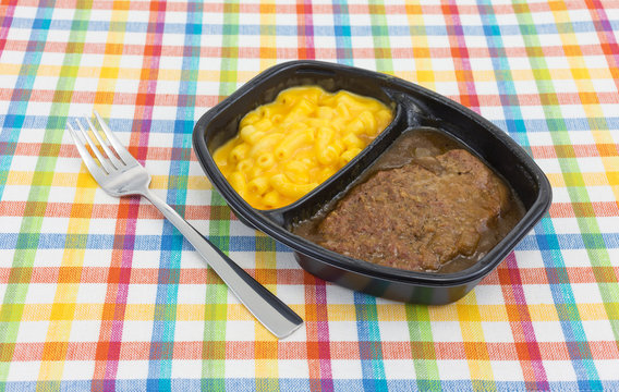 Salisbury steak meal with macaroni and cheese TV dinner with a fork to the side atop a colorful tablecloth.