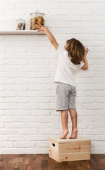 Cute little boy reaching for the cookies on the kitchen shelf © rangizzz