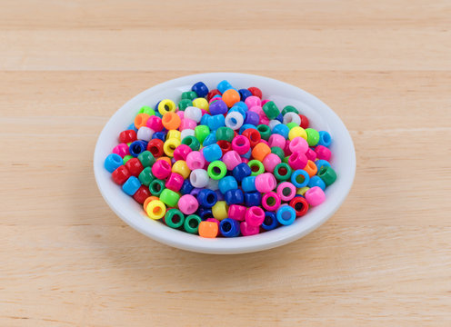 Pony beads in a small bowl on a wood table.