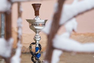Obraz na płótnie Canvas Big hookah for tobacco made of metal, glass and ceramics. Snowing. Snow background. White