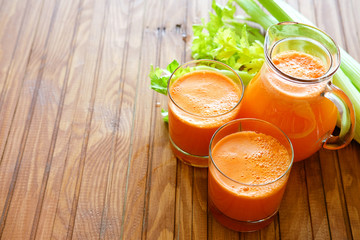 Fresh carrot juice poured into glasses and green celery