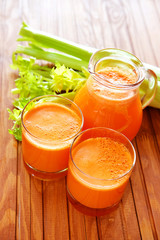 Fresh carrot juice poured into glasses and green celery