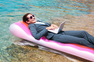 Happy businesswoman using laptop on pool raft