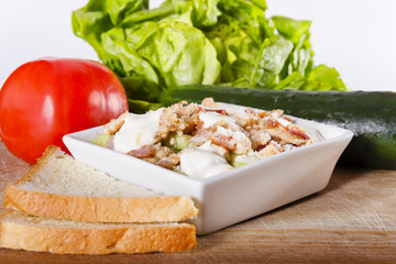 Simple, fresh salad with vegetables, grilled chicken and smoked ham in white bowl on a wooden board next to toast, cucumber and tomato, 