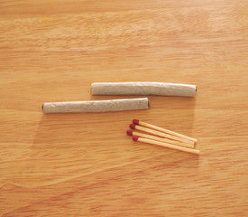 Horizontal photo of two Marijuana cigarettes and matches on wood grain table