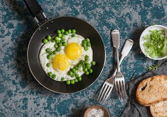 Delicious breakfast - fried eggs with green peas. On a dark background, top view