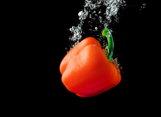 Red paprika pepper falling into the water with a splash and air bubbles. Healthy food on black background. Wash vegetables.