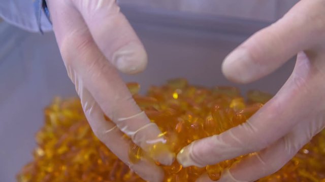 A pharmaceutical factory worker is having yellow pills in his fingers and then they are slipping through his fingers back in the plastic bag.
