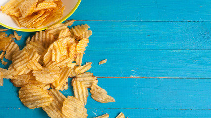 Potato chips poured out of the plate on a blue wooden table