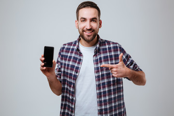 Bearded man showing blank smartphone screen and pointing at him