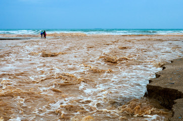 Muddy Rainwater washing away sand on a beach and merging with the sea after a storm