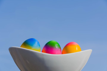 Bunt gefärbte  Eier in weißer Schale vor einem blauen Himmel