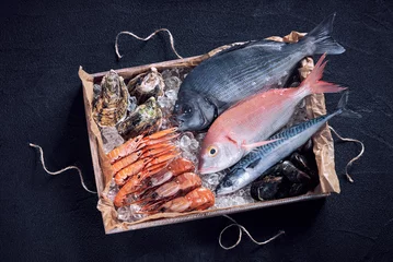 Foto op Plexiglas Vis Verse Spaanse vis en zeevruchten in houten kist op zwarte stenen tafel