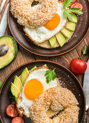Bagel with avocado and egg on the wooden background.